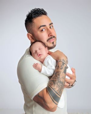 Tattooed father holding sleeping newborn baby against his chest in studio portrait.