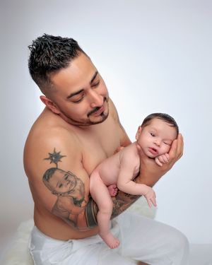 Shirtless tattooed father holding awake newborn baby in professional studio photo.