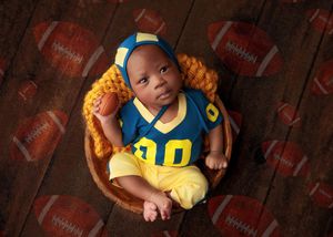 Newborn baby dressed in blue and yellow football uniform posed in a wooden bowl with football backdrop.