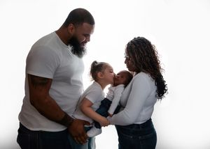 Family of four with parents and two young children sharing a tender moment against a white studio background.