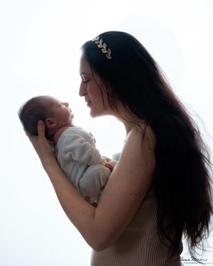 Silhouette of a mother with long dark hair smiling at her newborn baby against bright white background.