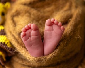 Close-up of tiny newborn baby feet resting on a soft brown textured blanket with colorful trim.