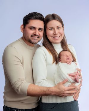 Happy parents in matching cream outfits holding their swaddled newborn baby during a studio portrait session.