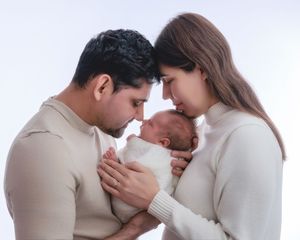 Loving parents touching foreheads together while gently holding their sleeping newborn baby between them.