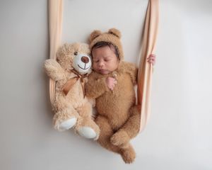 Newborn baby in bear outfit sleeping in a swing with a teddy bear.