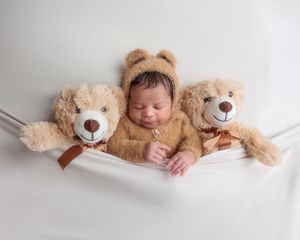 Smiling newborn in bear bonnet and outfit nestled between two teddy bears.