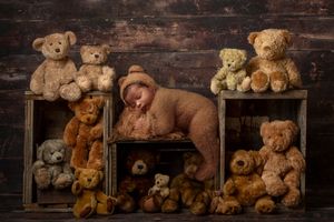 Sleeping newborn in bear bonnet surrounded by teddy bears in rustic wooden crates.