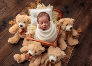 Swaddled newborn sleeping in a tiny wooden bed surrounded by teddy bears.