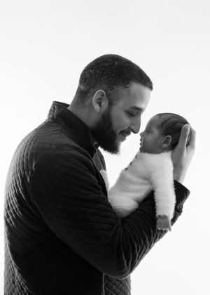Black and white photo of a bearded father tenderly holding his newborn baby close.