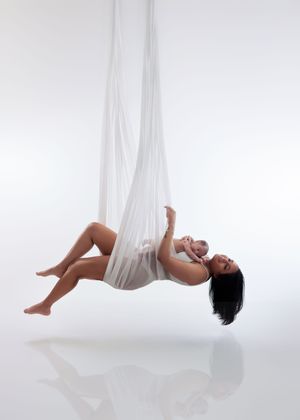 Mother and newborn baby posing together on aerial white silk fabric in a studio.
