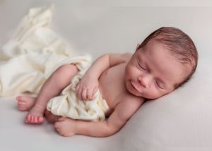 Smiling sleeping newborn baby posed on a soft white blanket in a professional photo.