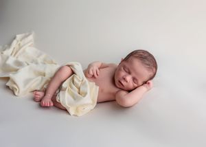 Peaceful sleeping newborn baby wrapped in cream blanket lying on white studio backdrop.