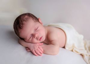 Peaceful newborn baby sleeping on hands on a soft white blanket in studio portrait.