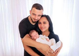 Happy young parents holding their sleeping newborn baby in a bright white studio portrait.