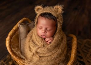 Newborn baby wrapped in brown knit and bear ear bonnet sleeping in a wicker basket.