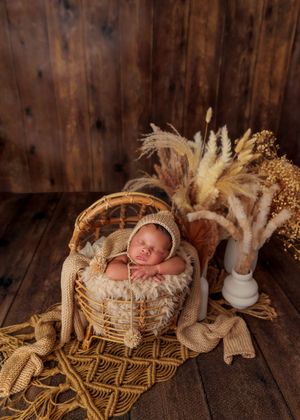 Peaceful newborn baby in a knit bonnet sleeping in a wicker basket with dried pampas grass decor.