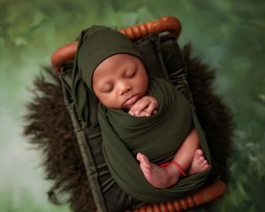 Sleeping newborn baby wrapped in green swaddle cloth and matching hat resting in a wicker basket.