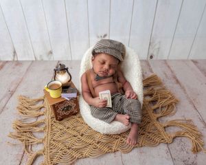 Newborn in newsboy cap and plaid pants posed with a mug and lantern.