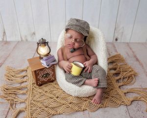 Newborn in newsboy cap holding a mug, posed with glasses and a lantern.