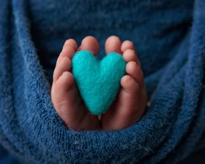 Newborn baby feet holding a teal felt heart wrapped in blue blanket.