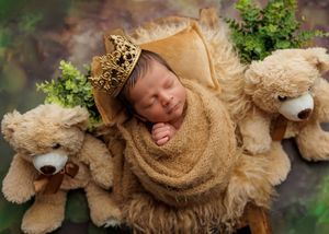 Sleeping newborn swaddled in brown wrap wearing a gold crown flanked by two teddy bears.