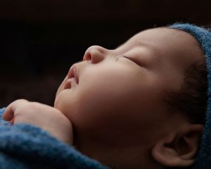 Close-up portrait of a sleeping newborn wrapped in a soft blue blanket.