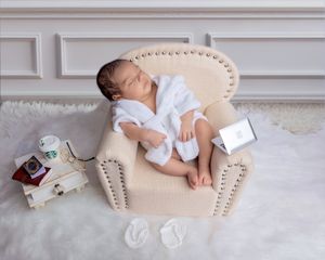 Newborn baby sleeping in miniature armchair with Starbucks and laptop props.