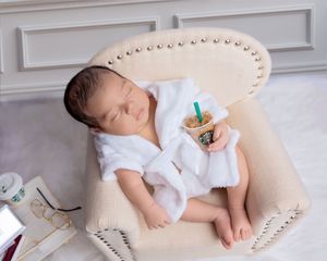 Sleeping newborn in white robe holding a Starbucks cup in mini chair.
