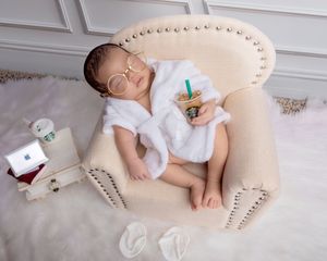 Newborn baby posed with glasses and Starbucks cup in tiny armchair.
