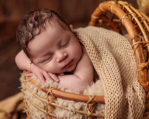 Sleeping newborn baby nestled in a wicker basket with soft beige knit wrap.