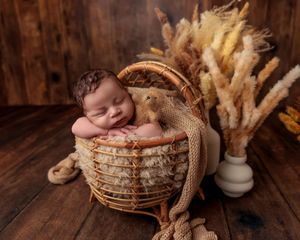 Peaceful newborn sleeping in a wicker basket with dried pampas grass decor.