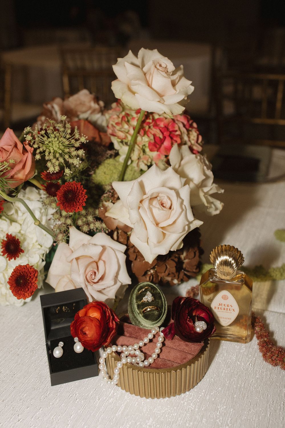 Vintage wedding details featuring delicate roses, antique trinkets, and jewelry arranged on a white textured surface.