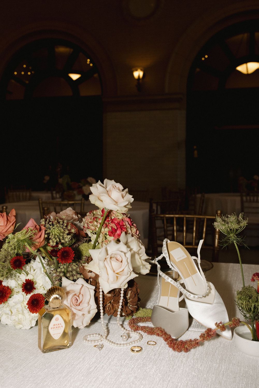 Wedding reception centerpiece with white roses, red flowers and decorative gold accents arranged on an elegant banquet table.