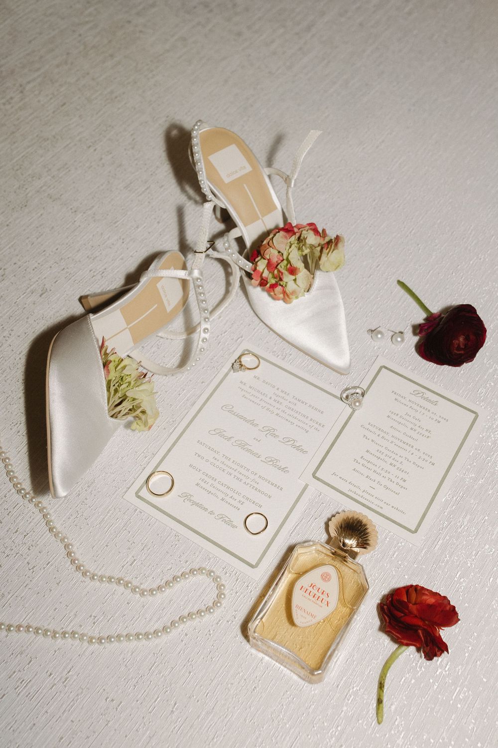 Elegant wedding invitation suite with pearl necklace and red roses on white textured background.
