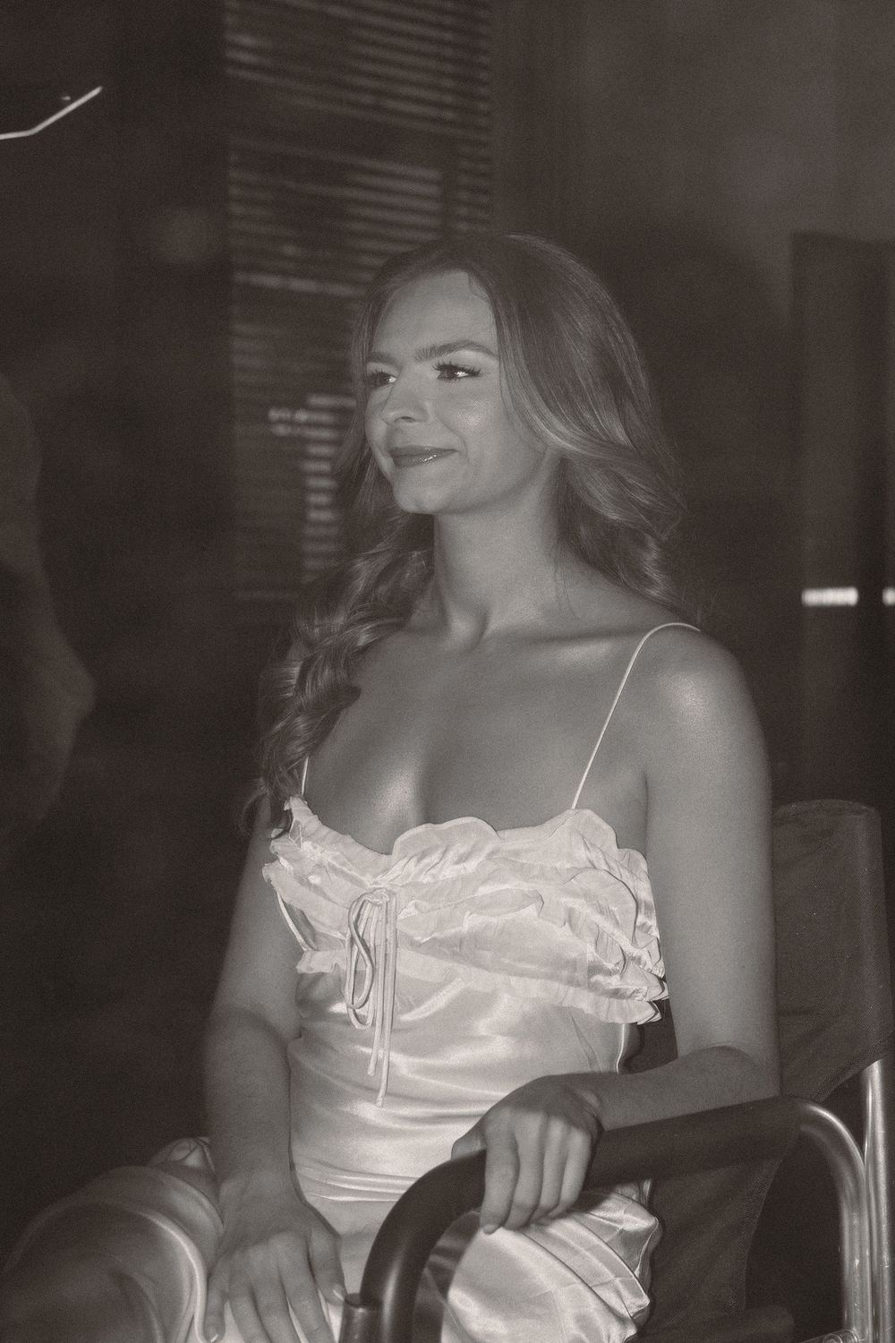 A black and white portrait of someone wearing a light-colored satin top sitting in a chair.