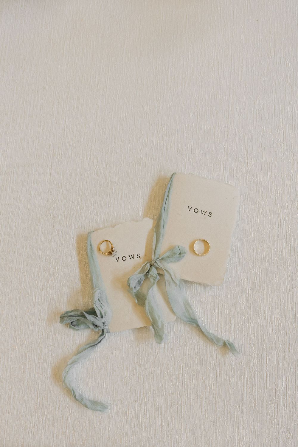 Delicate silk ribbon tied to a cream-colored vows card on a neutral textured background.