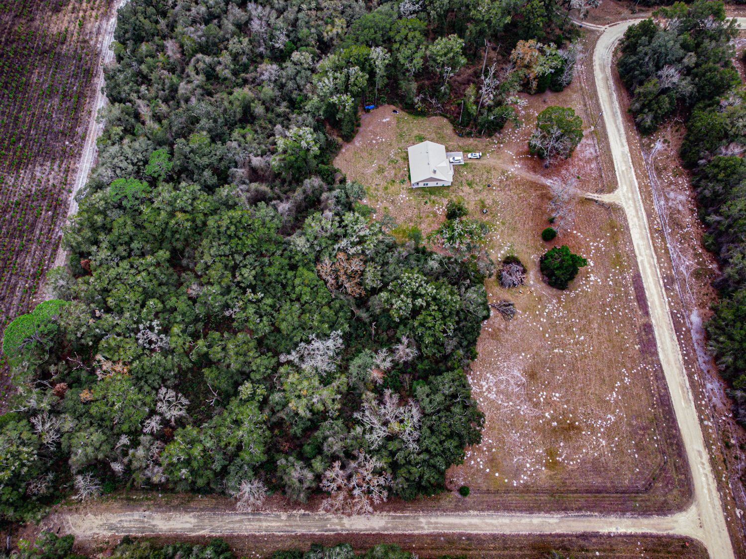 Aerial view of a rural property with dirt roads and wooded areas surrounding cleared land plots.