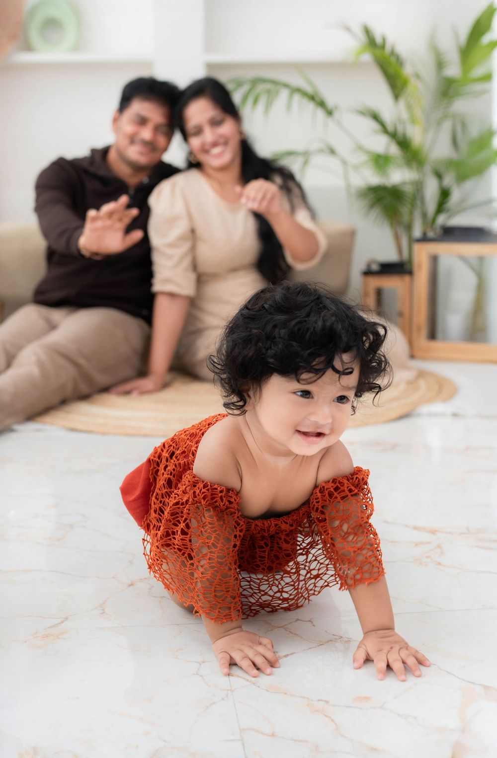 Toddler crawling on floor with parents in background during studio family toddler photoshoot in Hyderabad