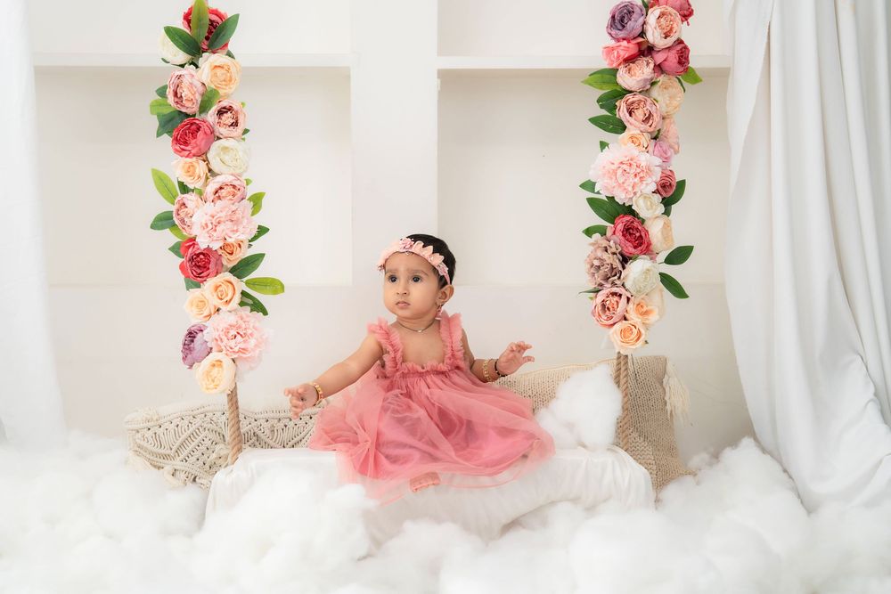 Toddler girl in pink dress sitting on floral swing during studio toddler photoshoot in Hyderabad