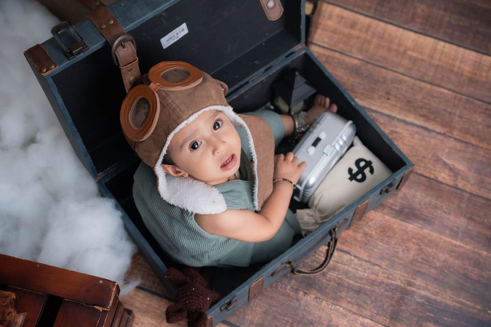 Toddler boy dressed as pilot sitting inside vintage suitcase during studio toddler photoshoot in Hyderabad