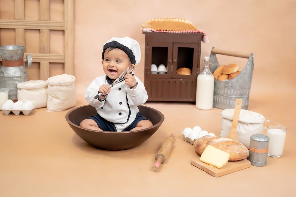 Toddler boy sitting in bowl with bakery theme props during studio toddler photoshoot in Hyderabad