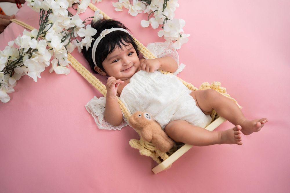 Smiling toddler girl lying on pink setup during studio toddler photoshoot in Hyderabad