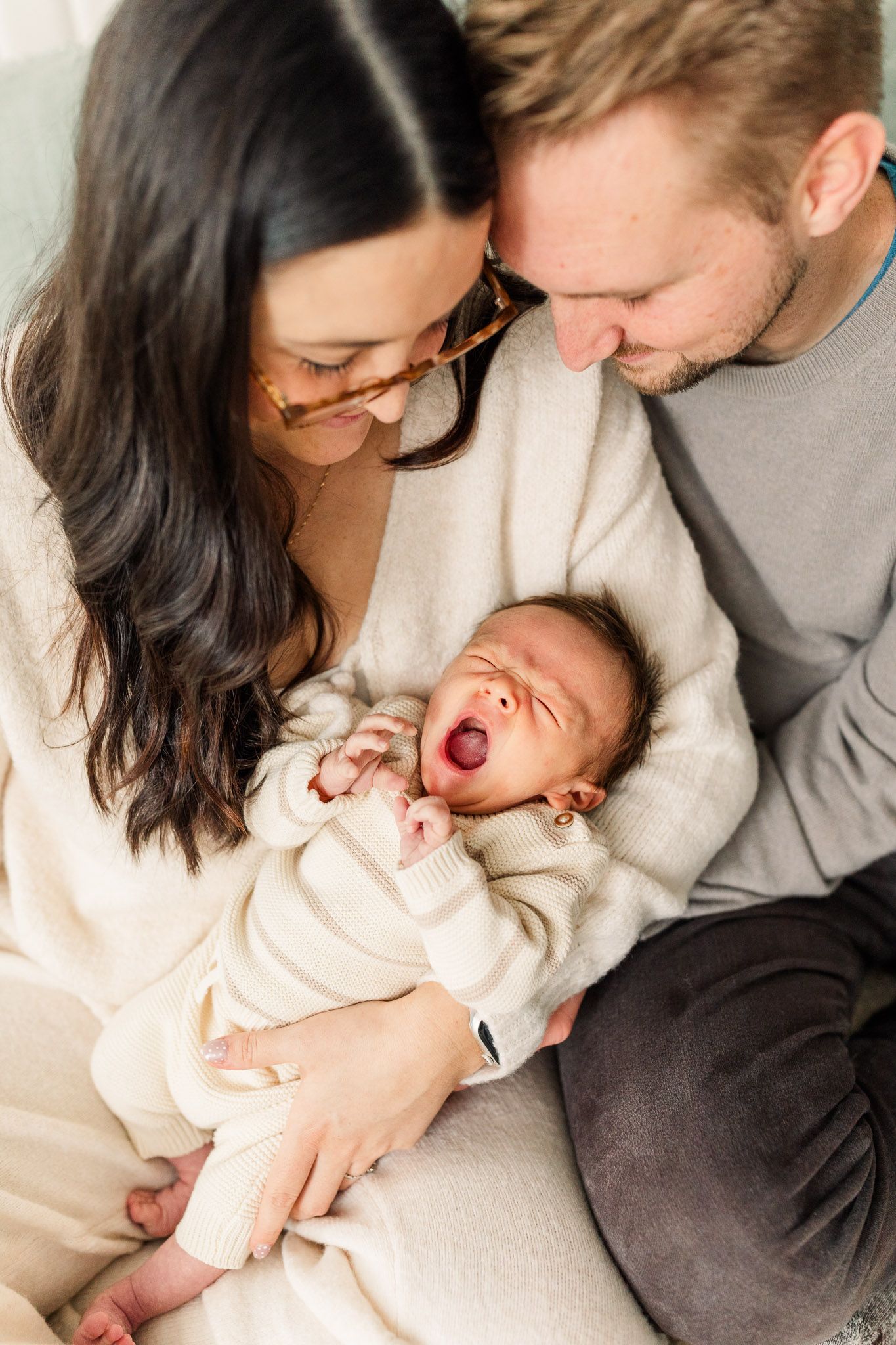 Baby yawns while mom and dad smile at him in their arms