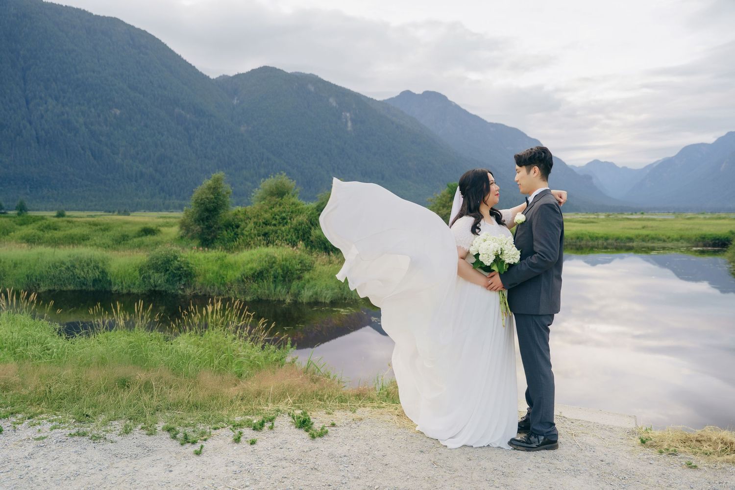 A couple shares a romantic moment against a backdrop of misty mountains and a serene lake in Alaska.