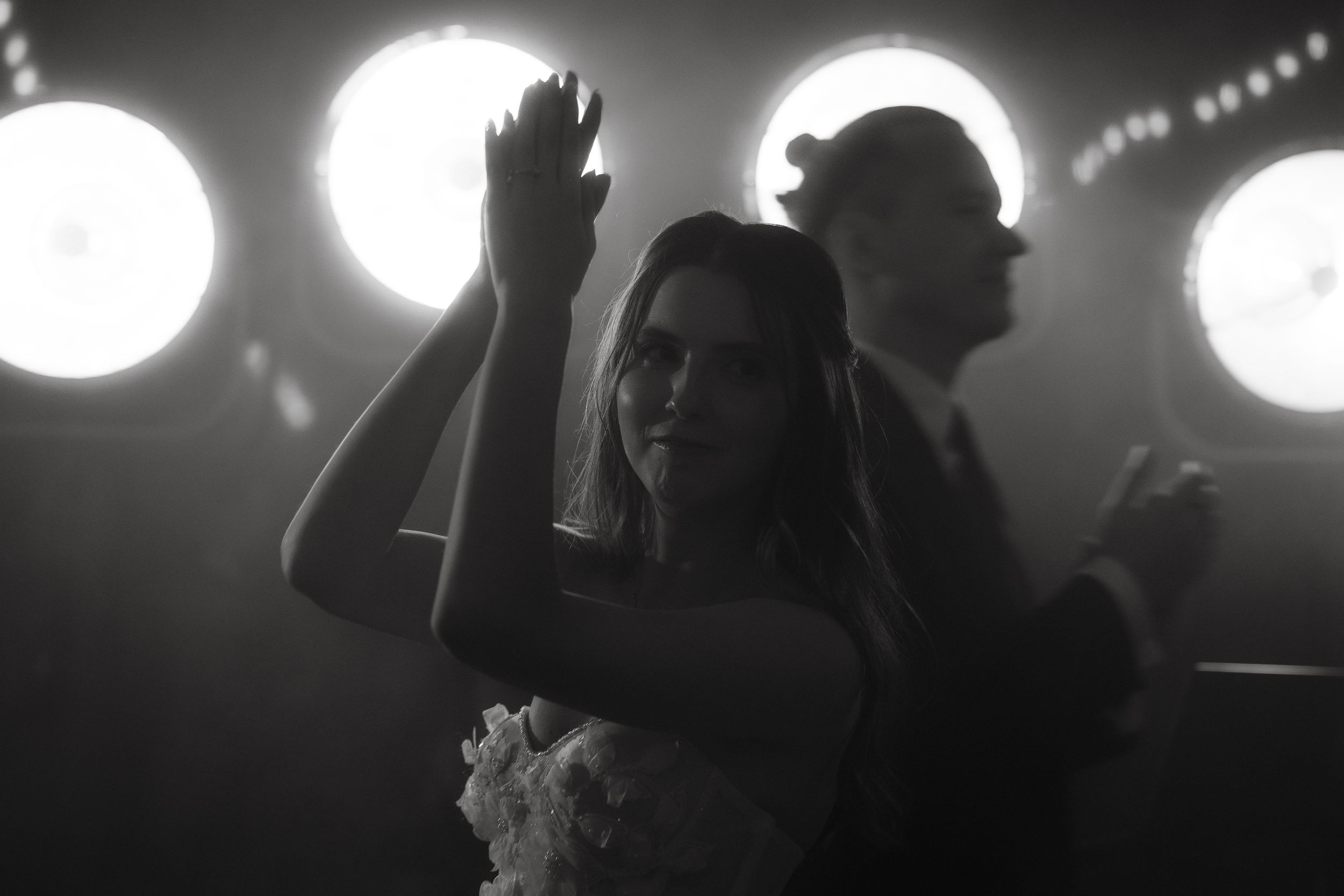 Black and white photo of people dancing at a nightclub with bright round lights in the background.