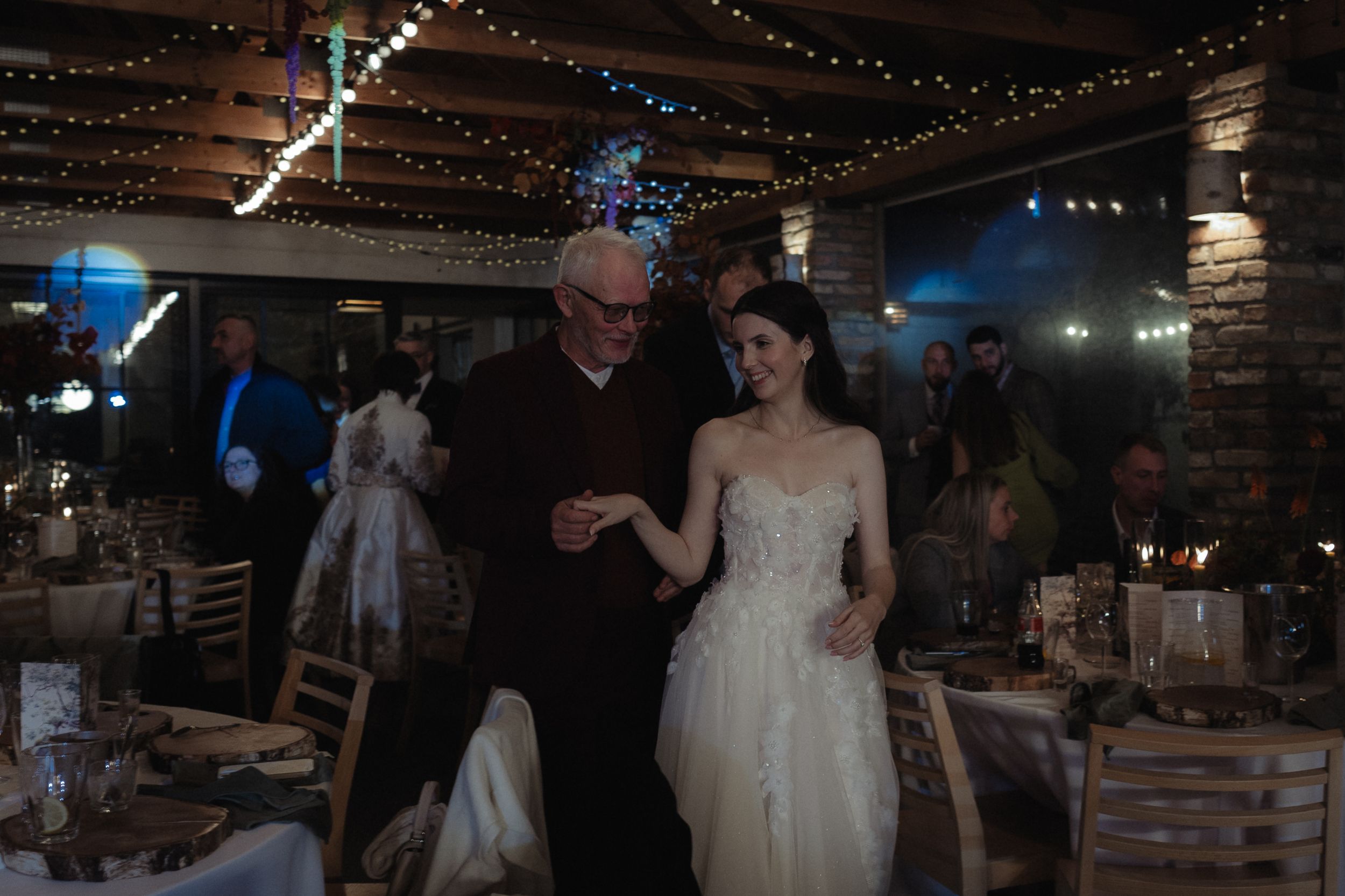 Dance floor at a rustic wedding venue illuminated by overhead string lights and blue spotlights.