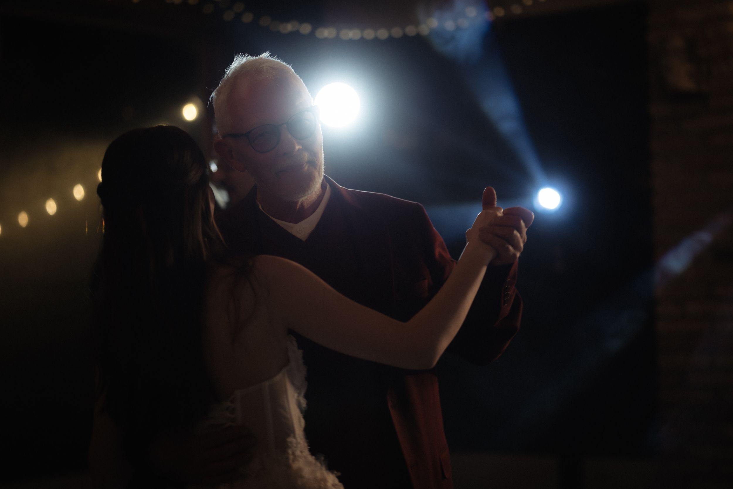 Silhouetted figures dance under a starry night sky with bright lights and illuminated decorations in the background.