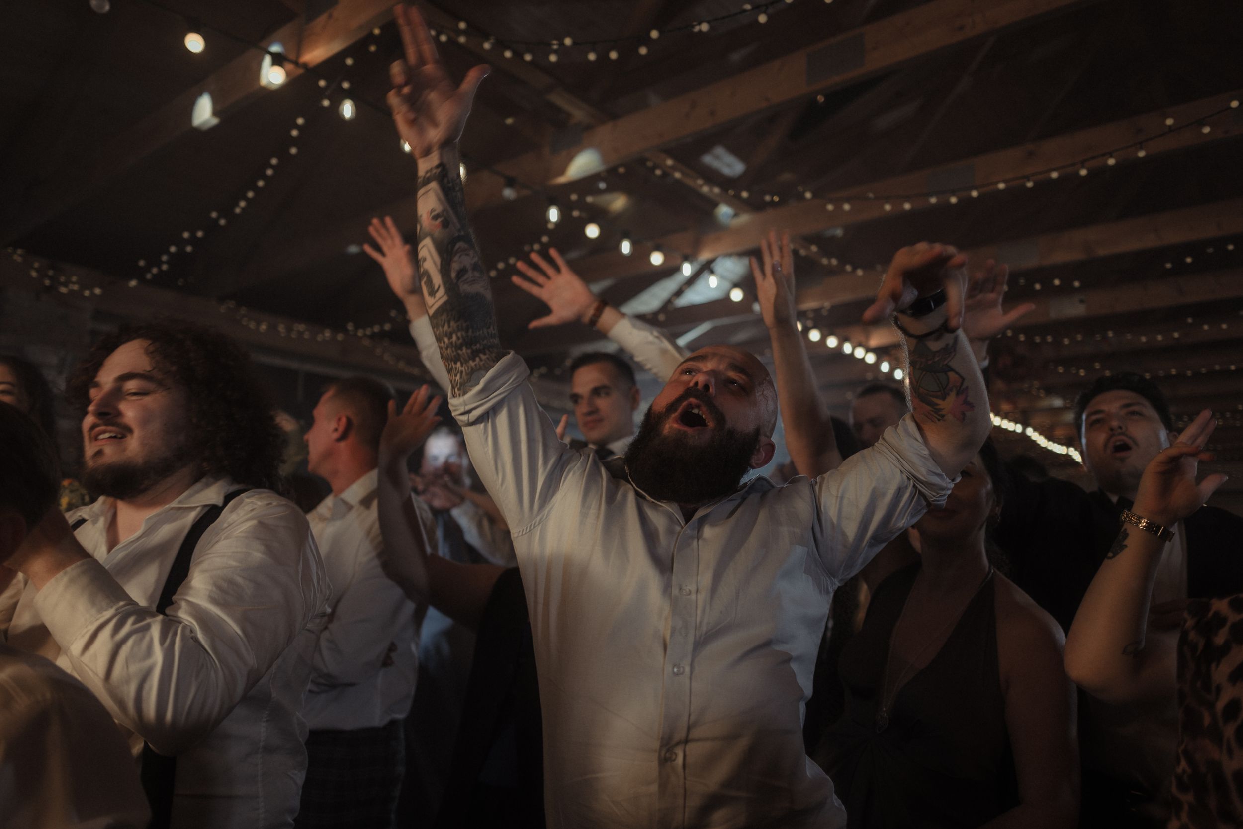 A group of people dancing and celebrating at a dimly lit indoor venue with string lights overhead.