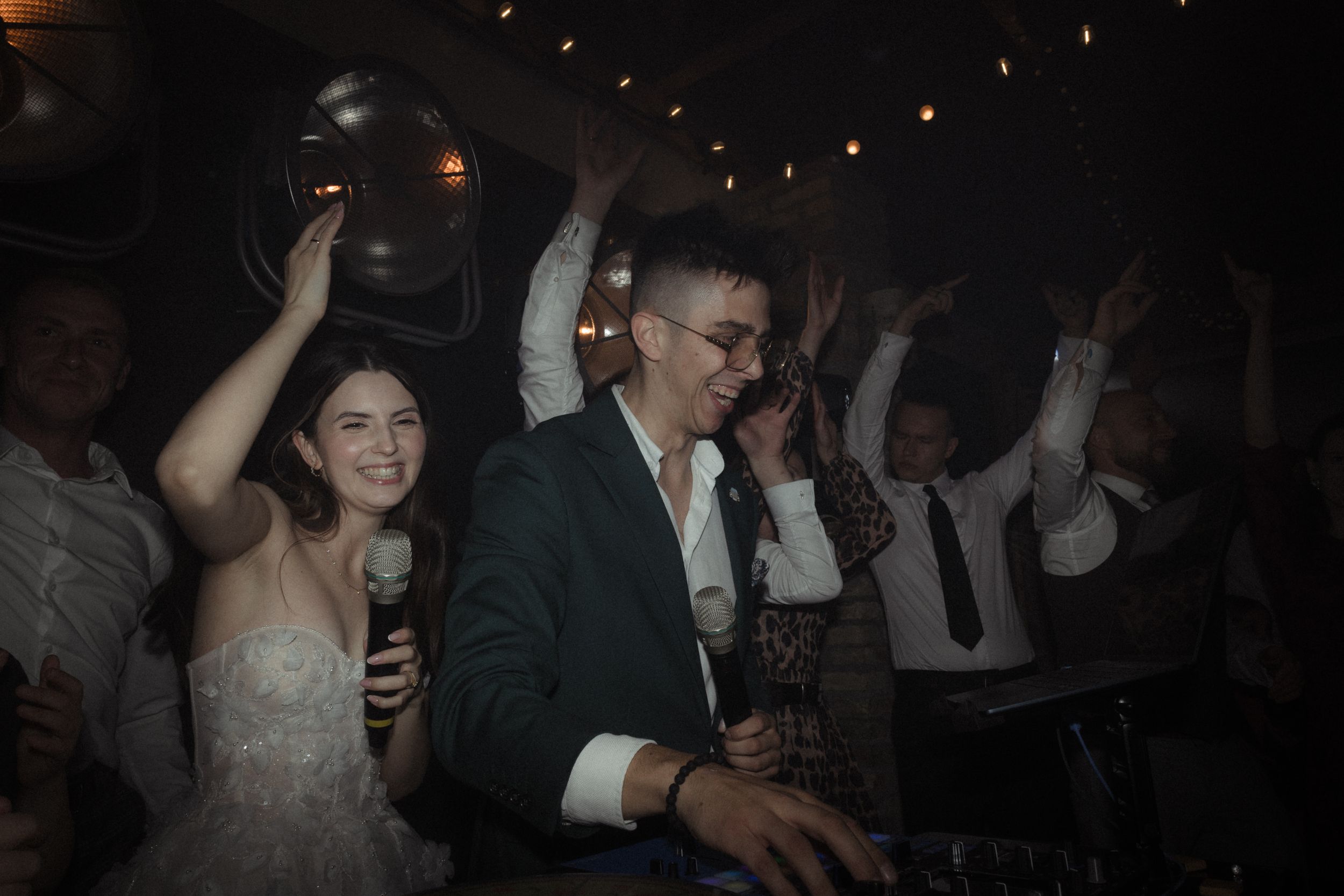Wedding reception guests dancing and celebrating on a dimly lit dance floor with warm ambient lighting.