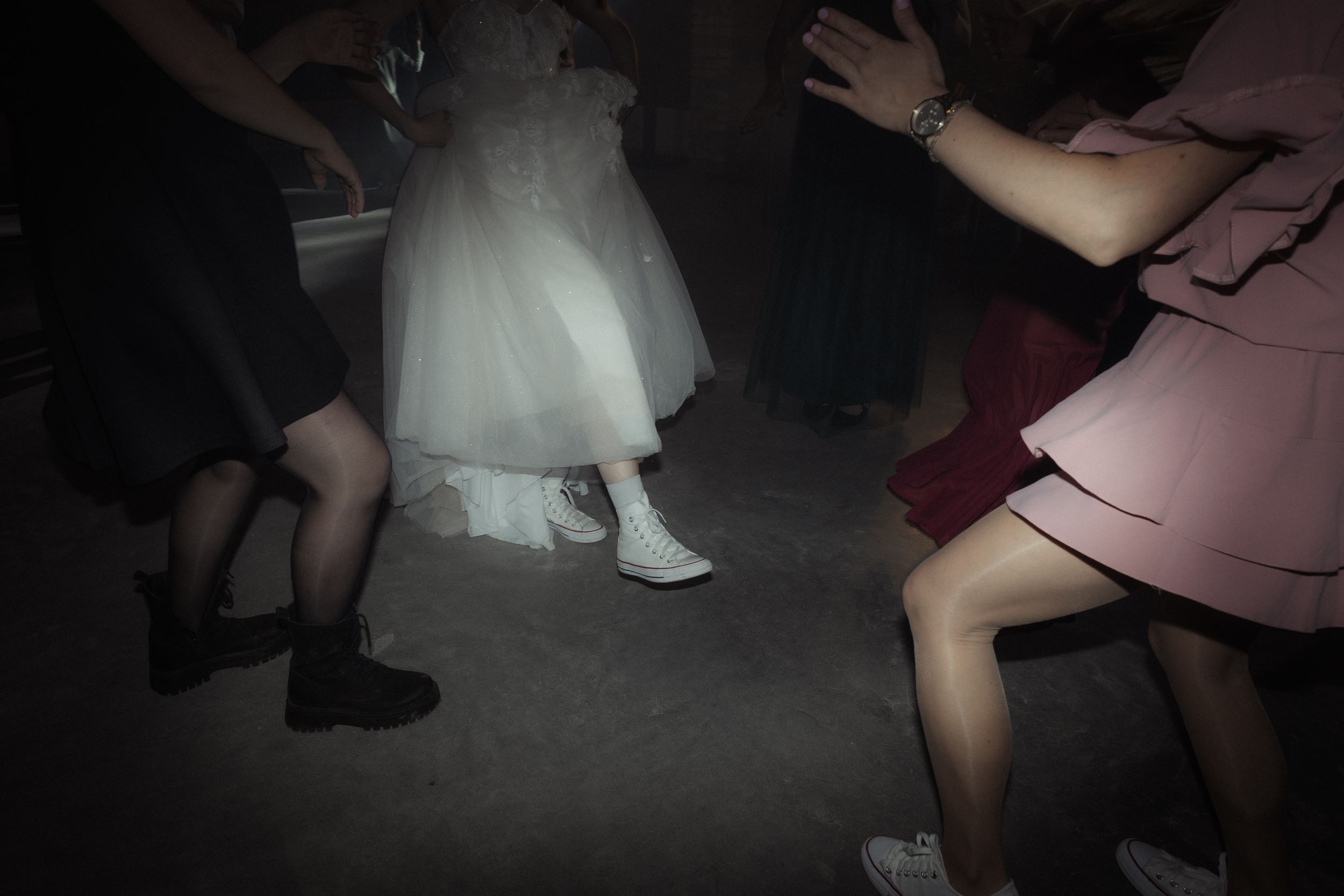 People dancing at a wedding reception with a white wedding dress visible in the dark lighting.